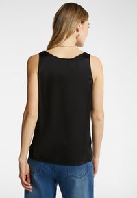 Top senza maniche in satin nero con scollatura a barca. Texture liscia e vestibilità comoda, abbinato a jeans di denim blu.