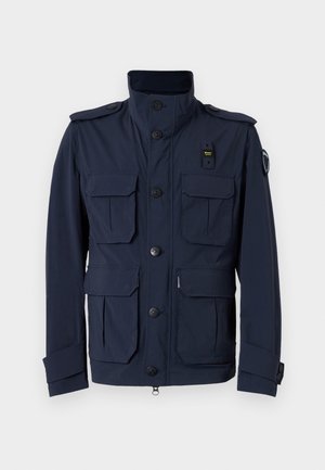 Casaco azul marinho com gola alta, múltiplos bolsos frontais, fechos de botão e épaulettes. Fabricado em tecido leve e texturizado.