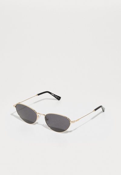 Gafas de sol de metal dorado con lentes ovalados, tintado gris oscuro, patillas delgadas y puntas curvas negras. Diseño ligero y minimalista.
