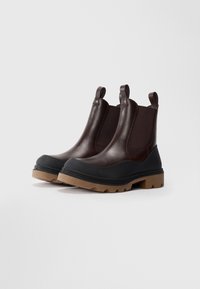 Bottes Chelsea en cuir marron avec inserts élastiques et languettes de tirage, dotées d'un pare-orteil en caoutchouc noir et d'une semelle extérieure rainurée beige.