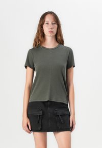 Olivgrön t-shirt med kort ärm och rundad halsringning, med rak sk�ärning. Kombinerad med en svart denimkjol med stora fickor.