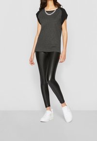 Grå och svart kortärmad topp med ett kedjehalsband, kombinerat med glänsande svarta leggings och vita sneakers. Slinig tyg och tight passform.