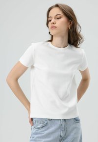 Witte T-shirt met korte mouwen, ronde hals en een gladde katoentextuur, gedragen met lichtblauwe spijkerbroek.