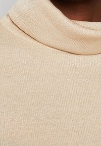 Beige coltrui van een zachte, geribbelde textuur met een subtiele glans, voorzien van een brede omgeslagen kraag en een snug fit voor het lichaam.