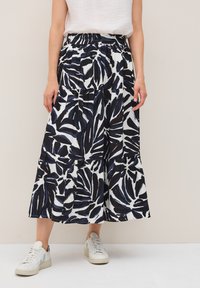 Jupe midi fluide à motifs bleu marine et blanc, ornée de motifs de feuilles audacieux, dotée d'une taille élastique et de couches superposées. Portée avec des baskets blanches.