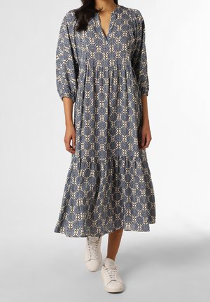 Femme portant une longue robe bleu et blanc à motifs, manches trois-quarts et baskets blanches, marchant en avant.