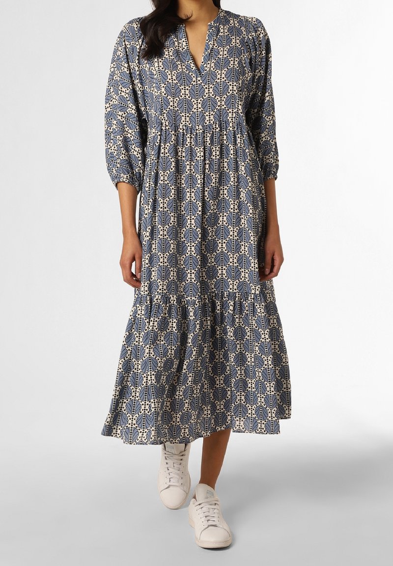 Femme portant une longue robe bleu et blanc à motifs, manches trois-quarts et baskets blanches, marchant en avant.
