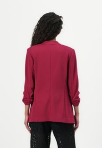 Blazer bordeaux au design ajusté, à manches longues et à col pointu. Tissu lisse avec une silhouette structurée et un détail d' ouverture au dos.