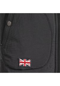 Schwarze Jacke aus strukturiertem Stoff, mit Reißverschluss, und einer Tasche mit einem gestickten Union Jack-Patch. Sichtbare silberne Hardwaredetails.