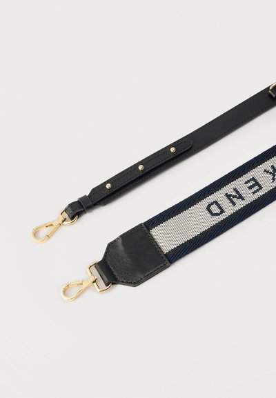 Ρυθμιζόμενοι ιμάντες τσάντας με χρυσά κούμπωμα, ο ένας από μαύρο δέρμα με τρουκς, ο άλλος από ναυτικό μπλε και λευκό ύφασμα με μερικώς ορατό κείμενο.