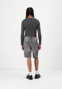 Chemise à manches longues grise associée à un short en jean gris. Le short possède une poche à l'arrière et deux poches arrière. Chaussures noires et chaussettes blanches visibles.