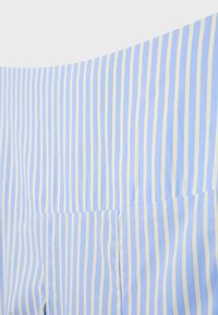 Tissu bleu clair avec des rayures verticales blanches et jaunes uniformément espacées et des coutures apparentes.