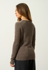 Brun ulltröja med rund halsringning, långa ärmar och ribbade muddar. Slät textur, figurnära design och små sidoklyvningar i fållen.