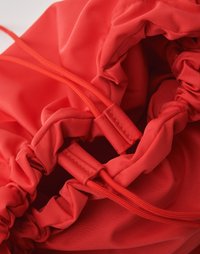 Sacchetto rosso con cordoncino realizzato in un tessuto liscio e lucido. Presenta bordi arricciati e due cordini rossi regolabili per la chiusura.