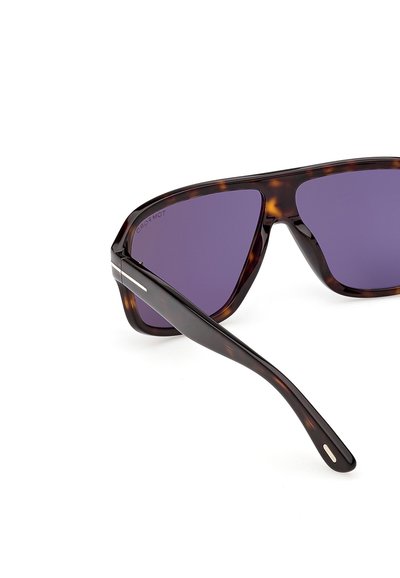 Lunettes de soleil en écaille avec des verres violets foncés, dotées d'une monture épaisse et de branches larges, sur fond blanc.