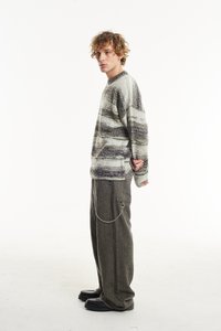 Pilkos ir kreminės bangos raštuoju megztas svarkas, derinamas su alyvuogių žalumo plačiomis kelnėmis, turinčiomis šoninės grandinės akcentą ir tekstūrinį apdailą.