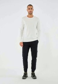 Hvid langærmet skjorte, sorte cargo-bukser med sidelommer og sorte sneakers. Casual pasform, glat tekstur og funktionelt design.