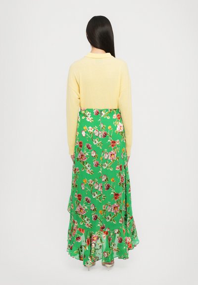 Top lavorato a maglia giallo con una texture morbida, abbinato a una gonna lunga floreale verde con orlo arricciato e vari motivi floreali colorati.