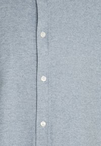 Camicia azzurra chiara con texture e patta dei bottoni con bottoni bianchi, che mostra un elegante motivo intrecciato su tutto il tessuto.