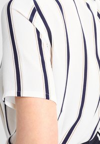 Bílá košile s vodorovnými námořnickými a béžovými pruhy. Krátké rukávy, texturovaná tkanina, volný střih, s kulatým výstřihem a detaily švů.