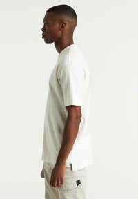 T-shirt bianco a maniche corte con collo a giro. Presenta fessure laterali e una trama sottile. Abbinato a pantaloni cargo beige chiaro.