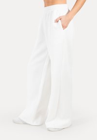 Pantaloni della tuta bianchi a gamba larga, realizzati in tessuto morbido, con vita elastica e tasche laterali, arricchiti da dettagli di cucitura discreti sui lati.