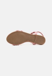 Pink sandal featuring a braided strap design, smooth texture, and a flat rubber sole with ridges for grip. Adjustable ankle strap.