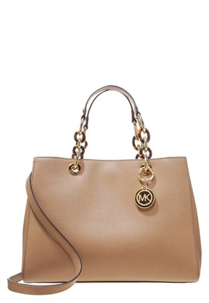 Sac à main en cuir beige avec poignées chaînes en écaille de tortue, ferrures dorées et un pendentif logo rond MK, avec une bandoulière amovible.