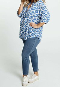 Blusa blu con motivo e vestibilità comoda, dotata di bottoni e maniche a metà. Abbinata a jeans blu slim-fit e sneakers bianche.