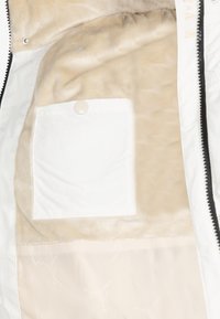 Insulated jacket interior featuring soft beige faux fur lining, a white fabric pocket with a button, and smooth cream lining with light patterns.