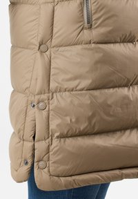 Beżowa kamizelka puchowa z pikowanym wzorem, zatrzaskami i bocznym zamkiem błyskawicznym. Posiada gładkie wykończenie materiału oraz lekko skrócony krój.