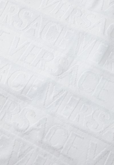 Valge rätik, millel on kõrgelt reljeefne tekst "VERSACE" ja tekstureeritud pind. Kanga välimus on pehme ja luksuslik, ühtlane värv.