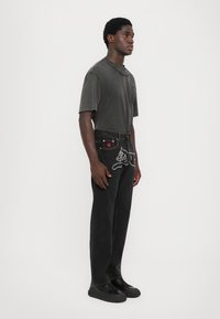 Svarte denim jeans med hvitt stikningsdesign som viser en katt. Grå oversized t-skjorte med rund hals, brukt sammen med svarte joggesko.