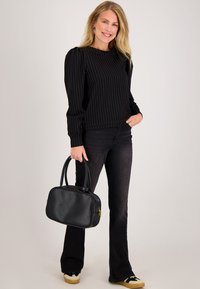 Zwart gestreepte trui met pofmouwen, gecombineerd met zwarte flared jeans. Houdt een gestructureerde zwarte leren handtas vast. Casual schoeisel zichtbaar.