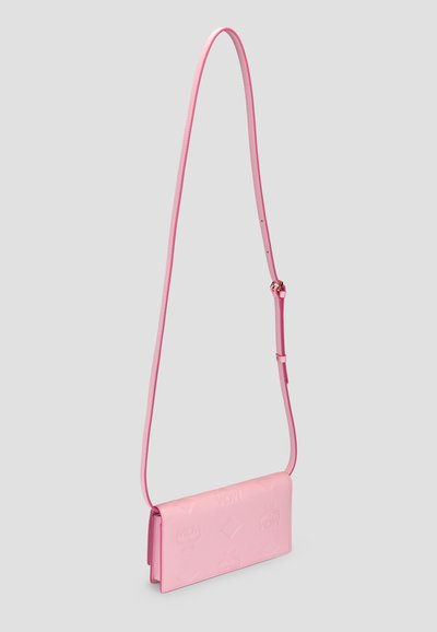 Ροζ δερμάτινη τσάντα χιαστί με ανάγλυφα λογότυπα και ρυθμιζόμενο λουρί σε απλό ανοιχτό γκρι φόντο.