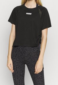 Kvinna som bär en svart cropped Puma T-shirt och högmidjade svarta leggings med ett mörkgrått ormskinnsmönster.