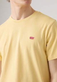 Camiseta de manga corta amarilla hecha de algodón suave. Presenta un pequeño parche con el logo rojo de Levi's en el pecho y un diseño clásico de cuello redondo.