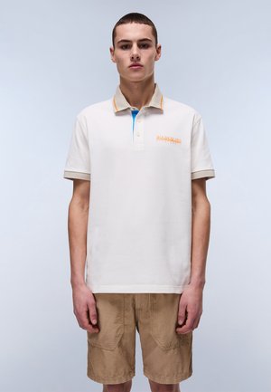 Cream polo shirt with orange and blue accents, featuring three buttons and embroidered logo. Worn with tan shorts, textured fabric.