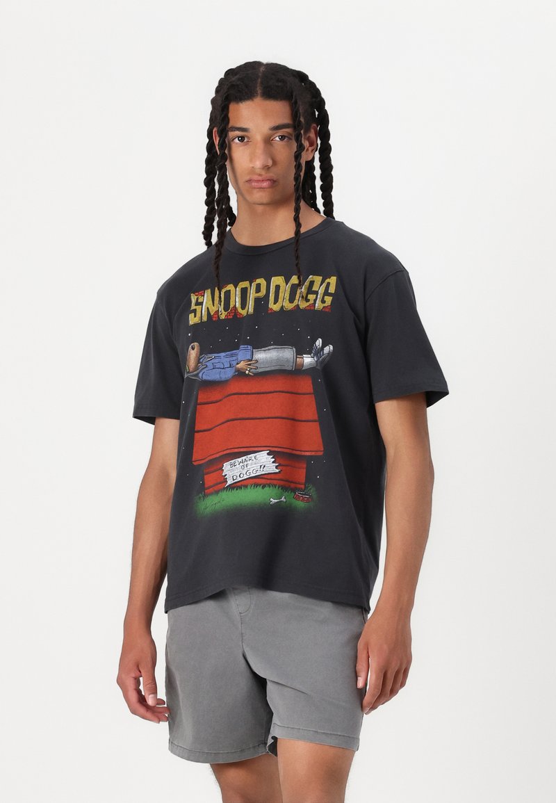 Sort bomulds t-shirt med et grafisk print af en tegneseriefigur på en hundehus, "Snoop Dogg" tekst med fed gul skrifttype. Korte ærmer, afslappet pasform.