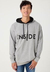 Sudadera gris con cordones negros y gran texto negro "INSIDE" en el frente. Cuenta con un bolsillo tipo canguro y una capucha negra en capas.