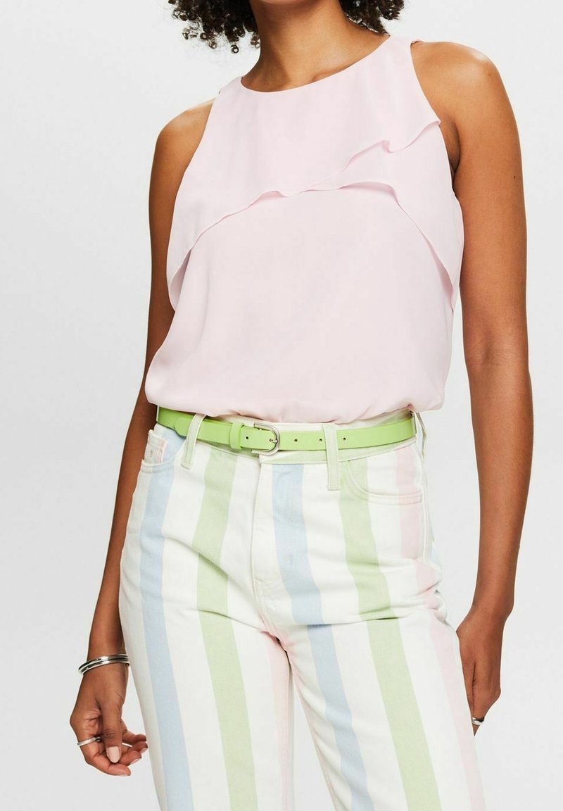 Femme portant un haut sans manches rose clair à volants et un pantalon taille haute à rayures pastel verticales avec une ceinture vert clair.