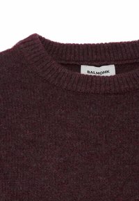 Bordeauxroter Strickpullover mit einem gerippten Rundhalsausschnitt. Weiche Textur und gleichmäßige Nähte, mit einem Etikett mit "BALMOHK" im Kragen.