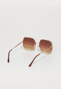 Ochelari de soare cu ramă din metal auriu, cu lentile octagonale, nuanță gradientă de maro și brațe cu model țestoasă. Nasere transparente pentru confort.