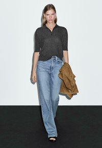 Grau gestricktes Poloshirt mit kurzen Ärmeln, hellblaue gerade Jeans und braune Wildlederjacke, getragen mit schwarzen offenen High Heels.