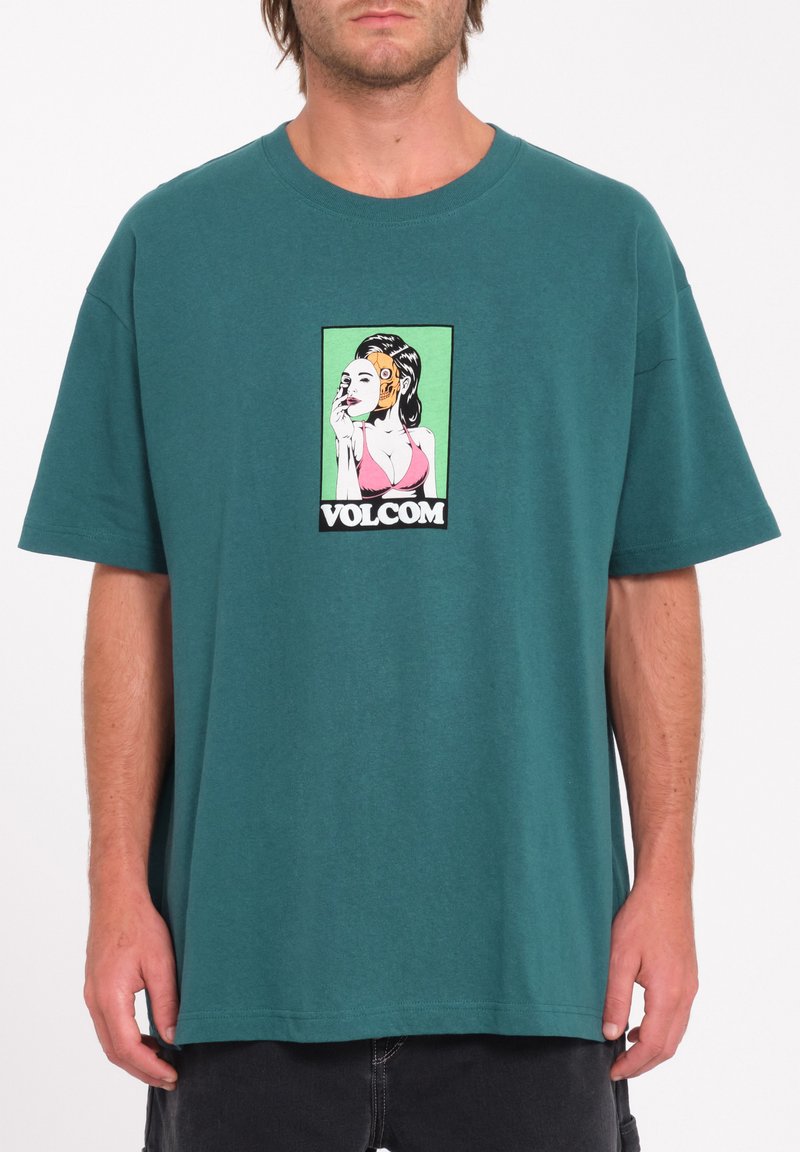 Turkusowy bawełniany t-shirt z odważnym nadrukiem przedstawiającym kobietę w różowym bikini, otoczoną zielonym tłem i czarnym napisem "VOLCOM".