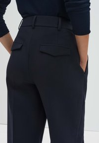 Pantalon habillé bleu marine avec une texture lisse, doté d'une coupe ajustée, de passants pour ceinture et de deux poches arrière à rabat.