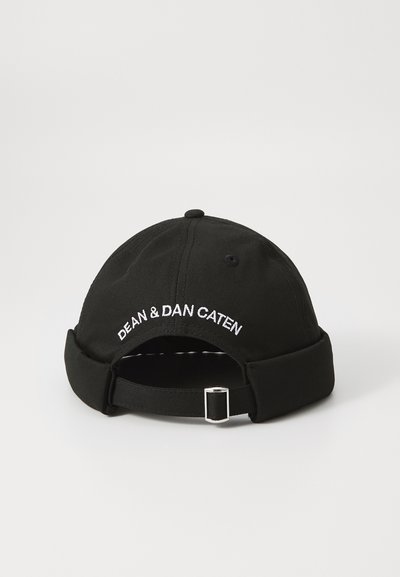 Black cap made of cotton with a curved brim. Features embroidered text "DEAN & DAN CATEN" in white. Adjustable strap with metallic hardware.