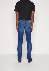Vaqueros de mezclilla azul oscuro con corte ajustado, que cuentan con un diseño de cinco bolsillos, costuras en contraste y un parche de logo de cuero en la cintura trasera.