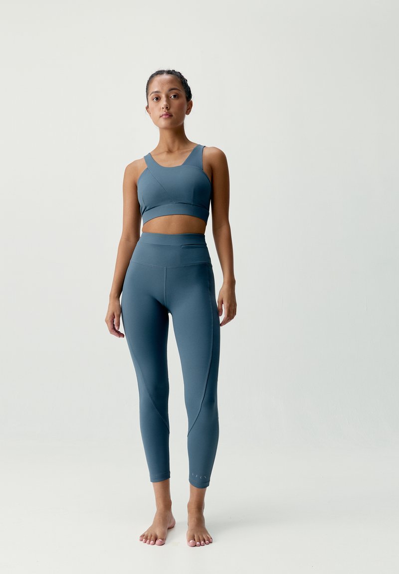 Sukienka sportowa w kolorze niebiesko-zielonym z pojedynczym ramiączkiem, w połączeniu z pasującymi legginsami o wysokim stanie, które mają kątowe detale szwów i elegancką fakturę.