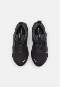 Sorte atletiske sko med teksturert overdel, snøring og reflekterende detaljer. Logoen vises i hvitt på siden. Polstret innside.